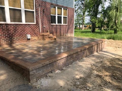 Newly paved patio area with interlocking stones beside a brick building and greenery.