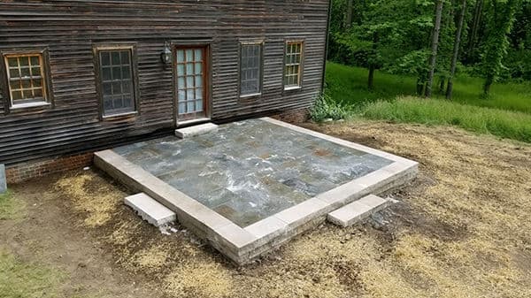 Slate patio installation adjacent to a wooden house with a grassy background.