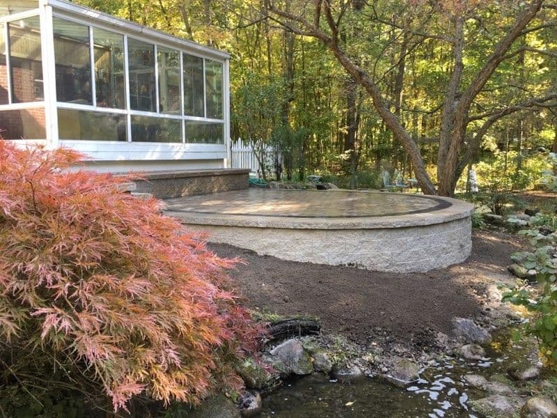 Patio installation next to a house, surrounded by trees and a vibrant garden.