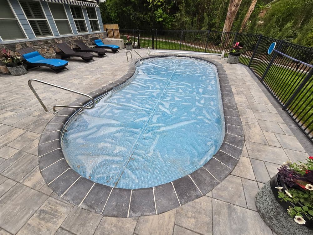 Modern backyard pool with a safety cover, surrounded by stone pavers and lounge chairs.