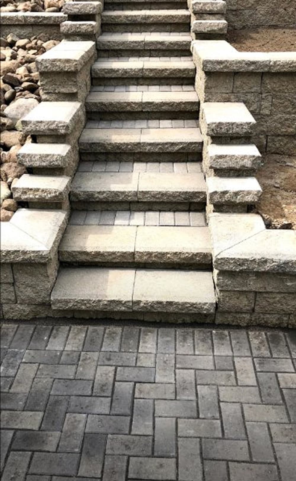 Stone steps leading up a decorative paver pathway with landscaped surroundings.