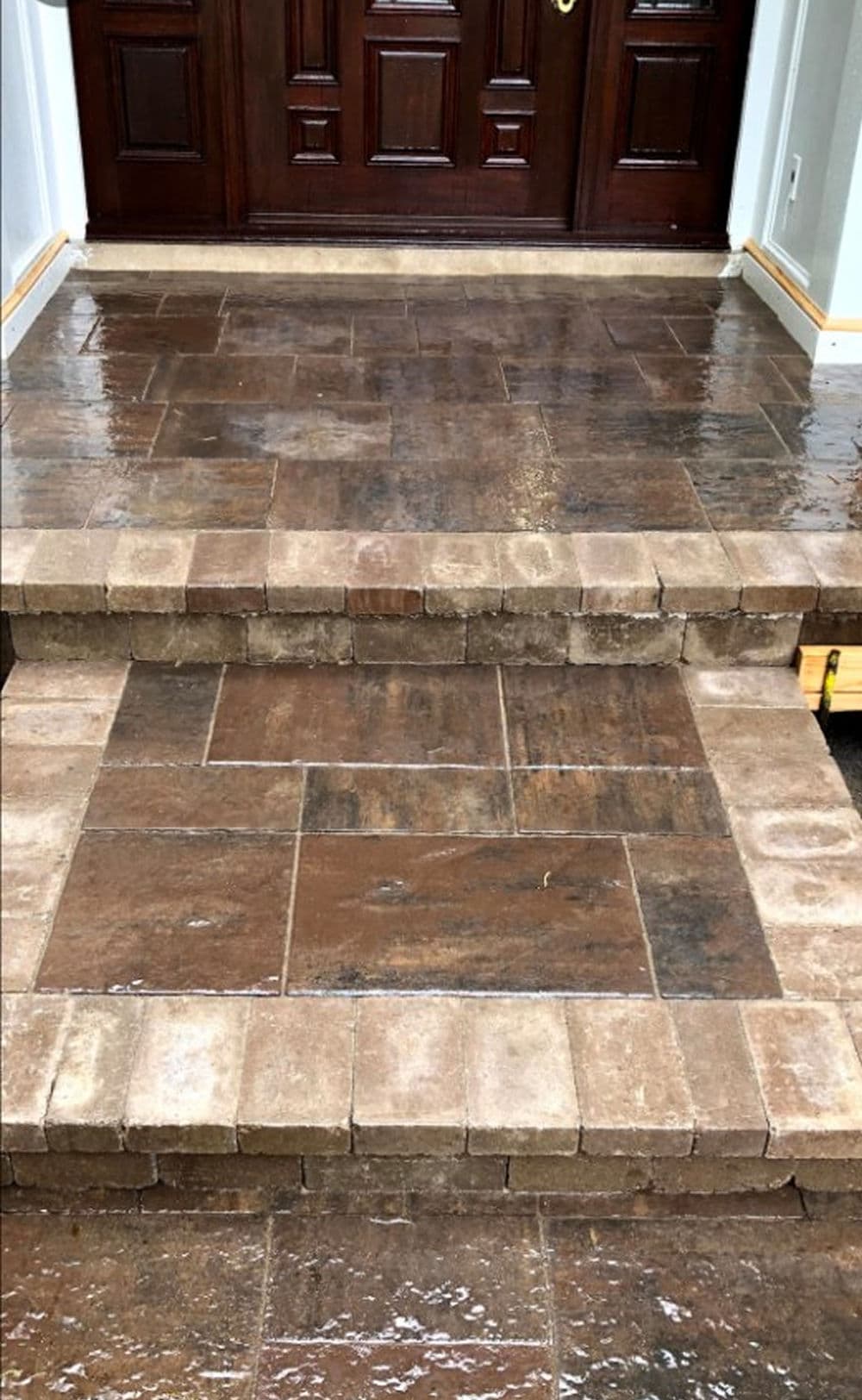 Newly installed brown stone paver steps leading to a wooden front door with glossy finish.