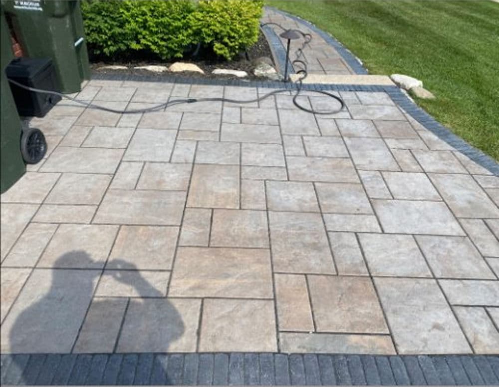 Patterned concrete patio with recycling bins and neatly edged landscaping. Clean and maintained.
