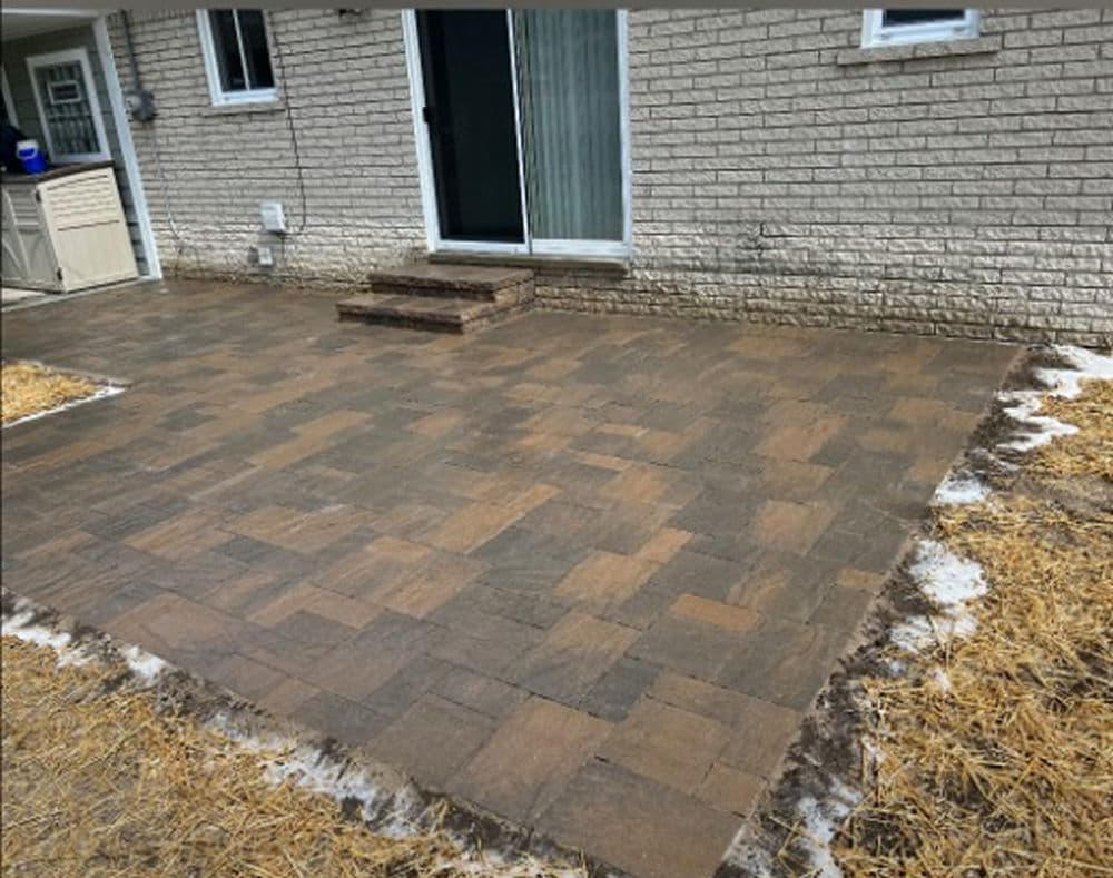 Newly installed textured patio with stone-like pavers, surrounded by straw and home entrance.