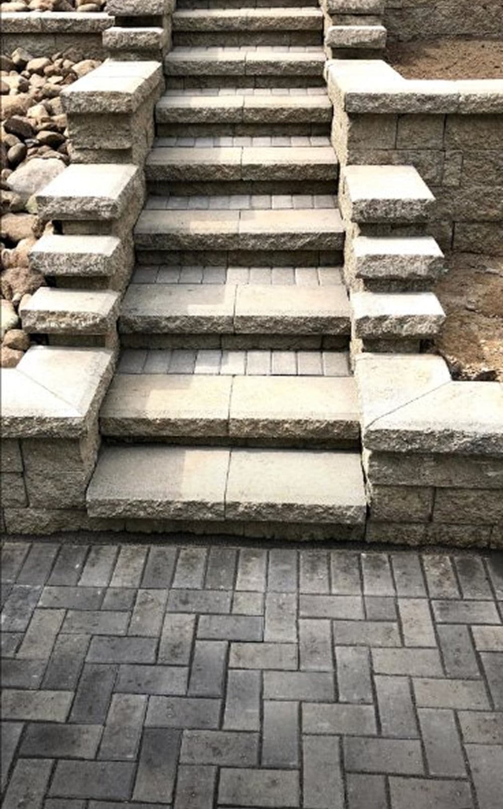 Stone steps leading up to a landscaped area, featuring textured pavers and a stone wall.