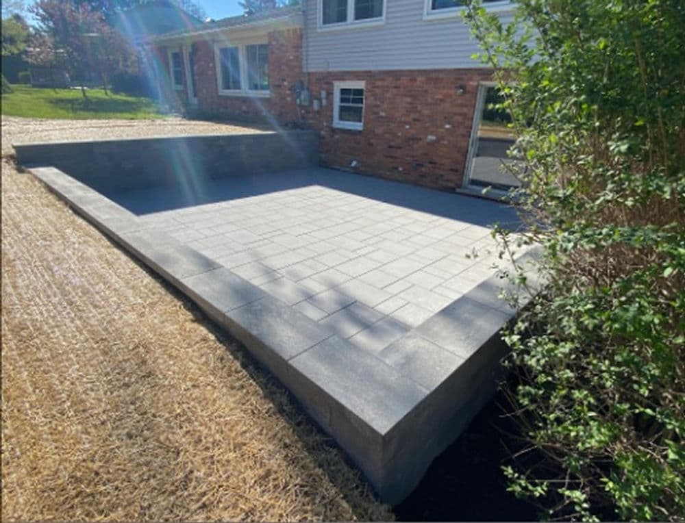 Newly installed stone patio with concrete border next to a residential home.