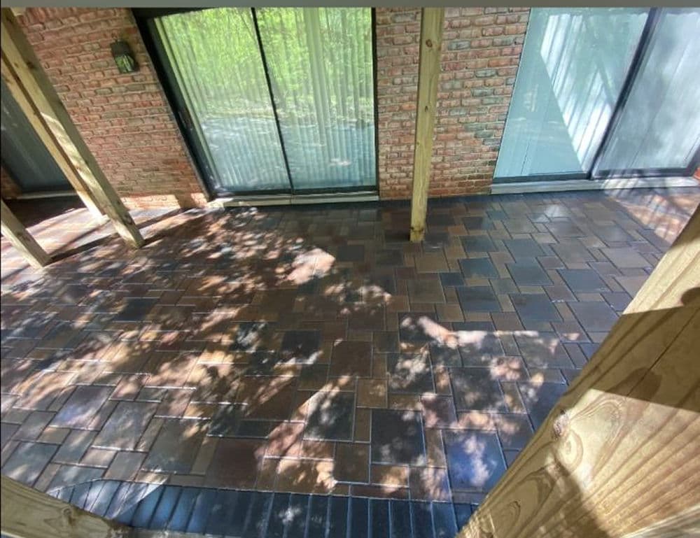 Paved patio with brick detailing and large windows overlooking a green landscape.