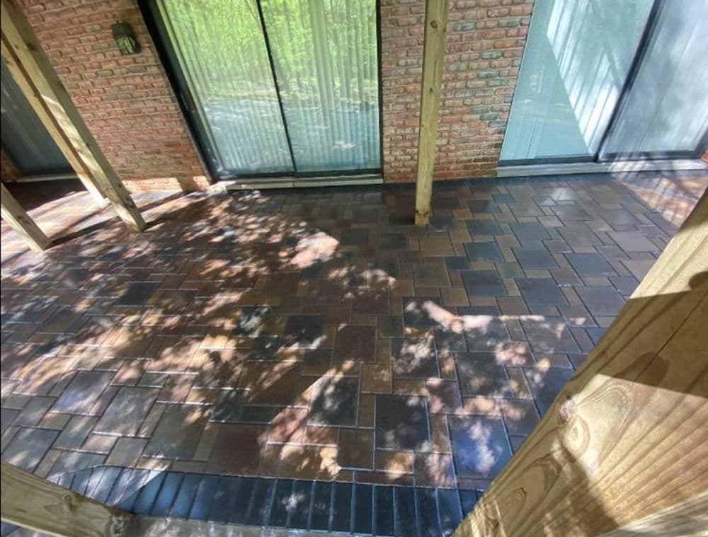 Paved outdoor patio with brick flooring and shadows from overhanging structure.