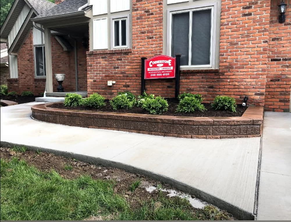 Home exterior with red brick, flower bed, and Cornerstone real estate sign in front yard.