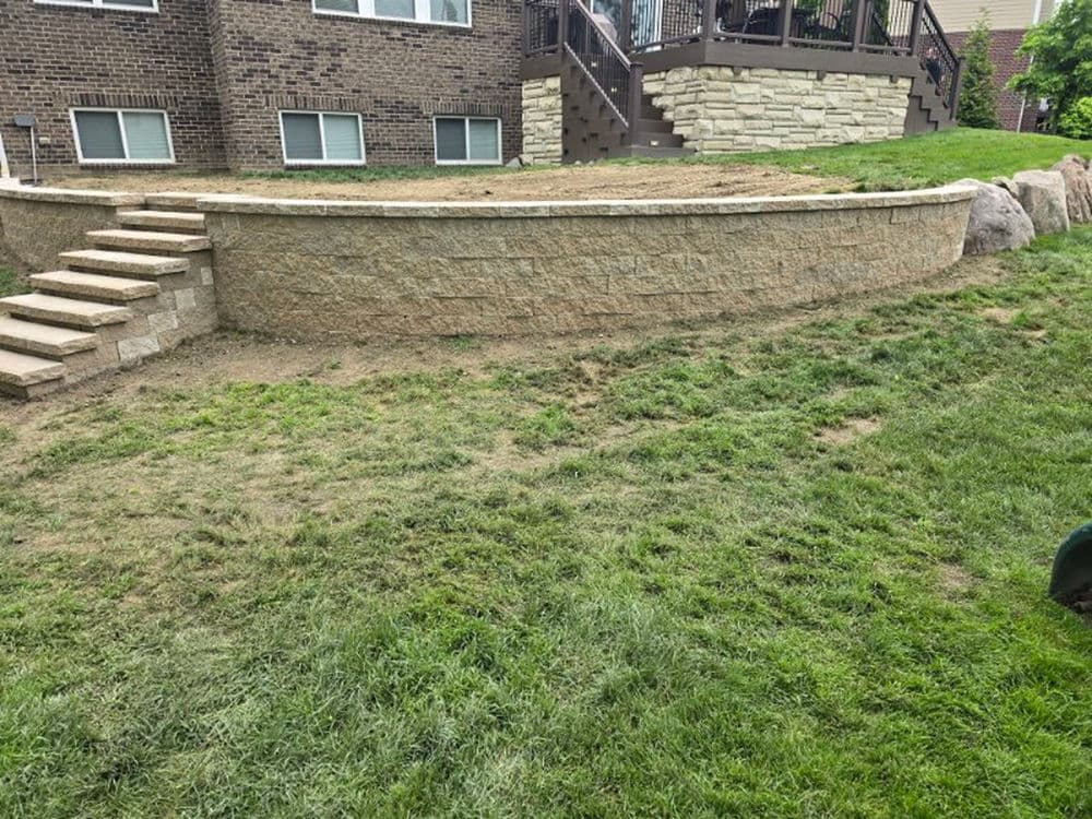 Landscape featuring a stone retaining wall and grass yard with steps leading to the house.